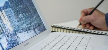 Person takes notes on a notebook next to a laptop